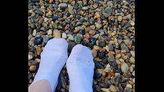 Playing with my feet in white socks with pebbles on the beach Thumb